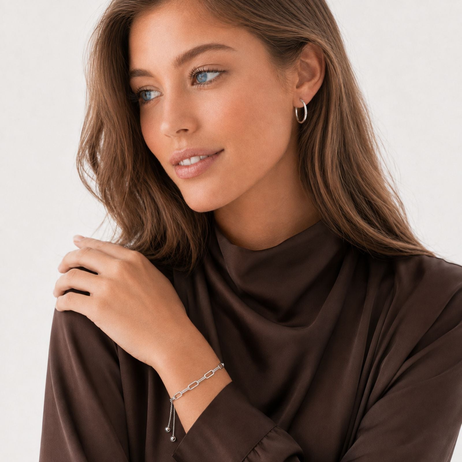A person wearing a long-sleeved beige top displays a bracelet with multiple amber or orange-colored gemstones set in a metal band on their wrist. Their hand is gently resting on their opposite shoulder.