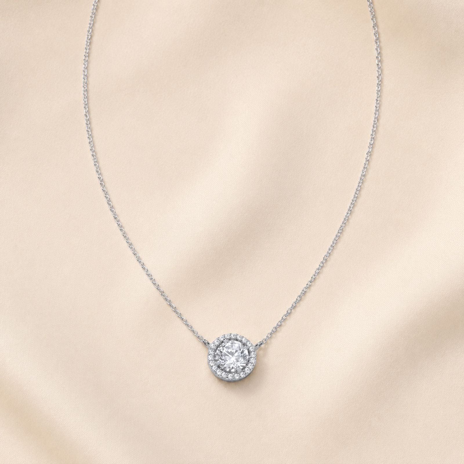 A woman wearing a taupe ruffled top and a round pendant necklace. The photo is cropped to show her from the shoulders to just above the chest.