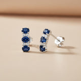 Silversmiths sterling silver drop stud earrings with simulated sapphire and CZ, displayed on a beige background.