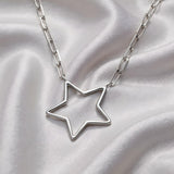 A Sterling silver paperclip chain necklace with an open star pendant rests on smooth light-colored satin fabric.