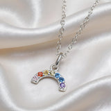 A sterling silver crescent moon necklace with rainbow cubic zirconia rests on white satin fabric.