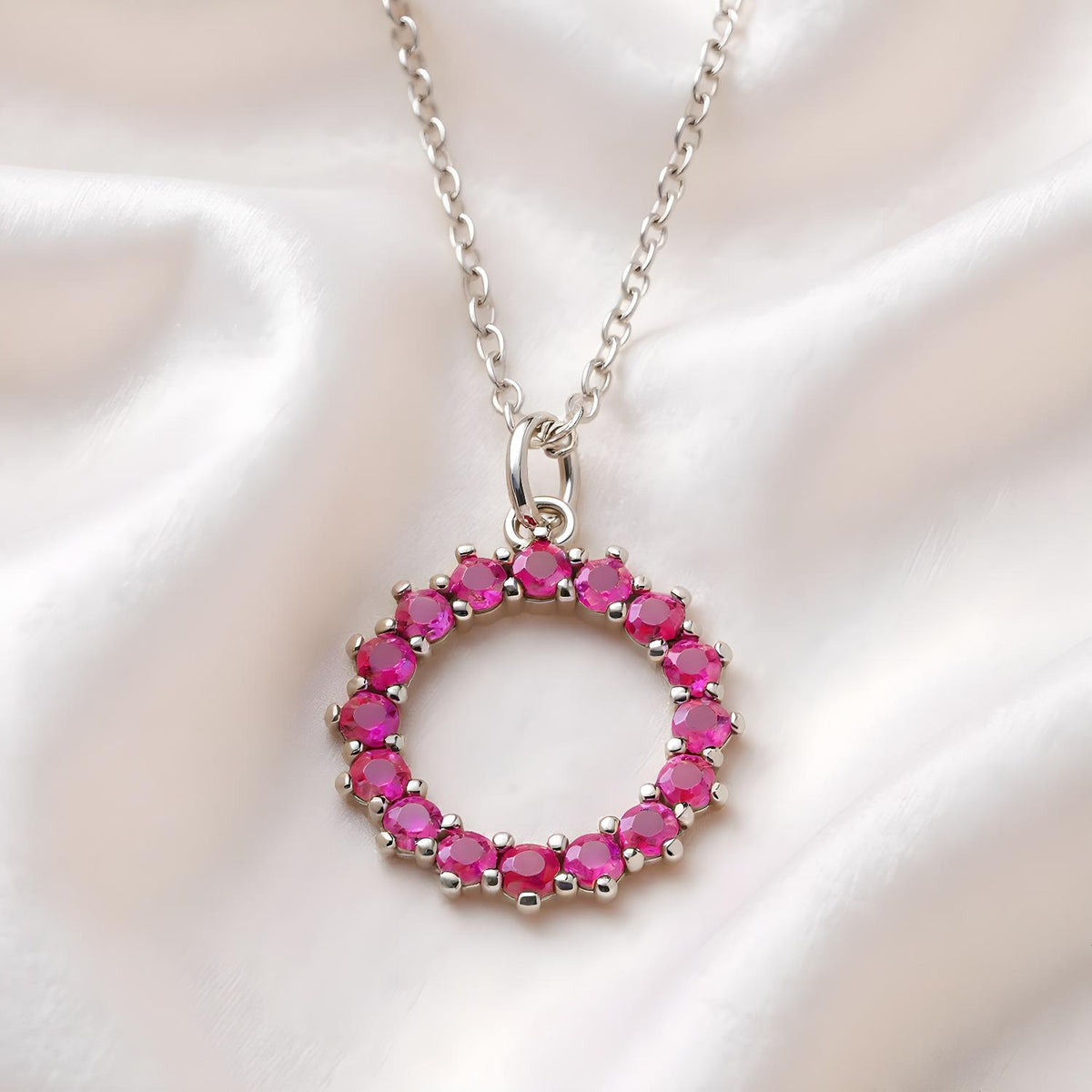 Silversmiths sterling silver necklace with a simulated ruby circle pendant rests on white satin fabric.