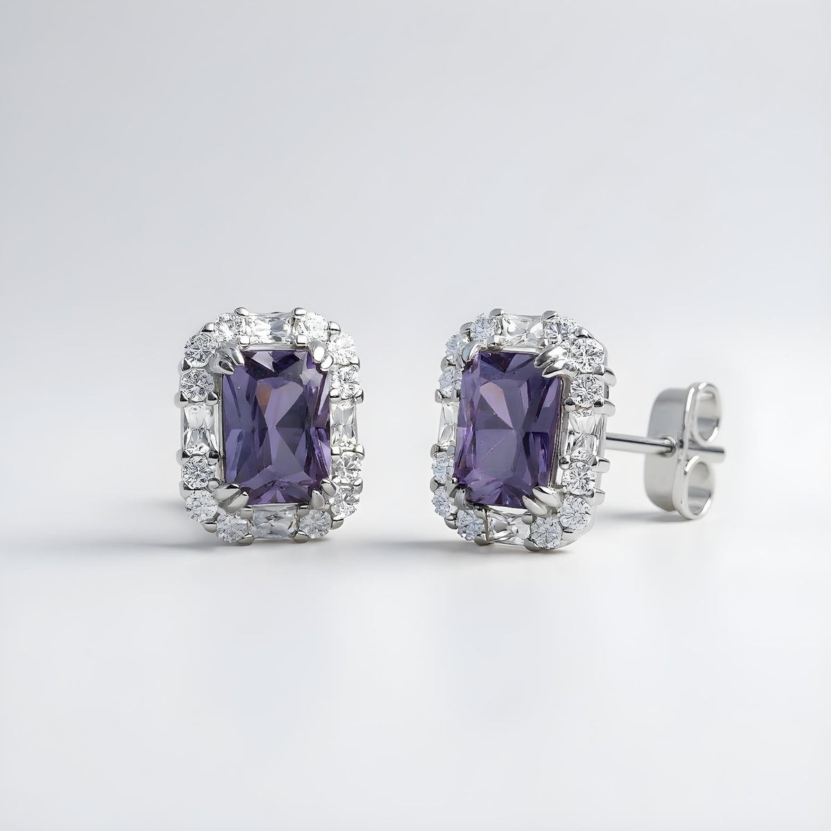 Emerald-cut simulated tanzanite halo stud earrings in sterling silver by Silversmiths on a plain background.