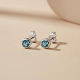 Silversmiths sterling silver stud earrings with simulated London topaz set in bezels on a smooth beige surface.