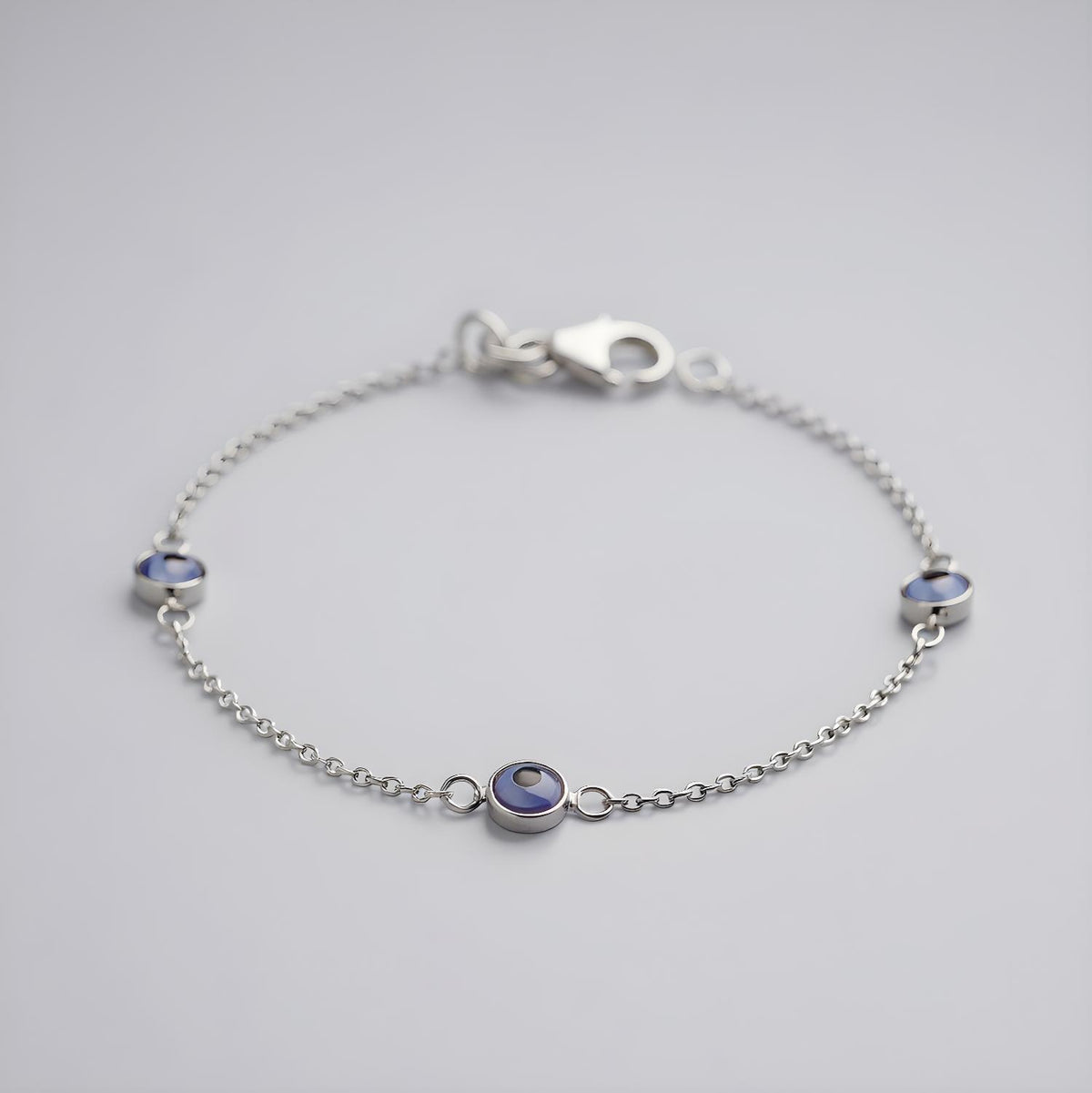 Sterling silver bracelet featuring three blue evil eye charms and a lobster clasp, displayed against a plain background.