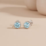Silversmiths sterling silver stud earrings with round blue topaz stones set against a beige background.