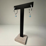 Silversmiths silver hoops with simulated aquamarine stones for March, shown on a black T-stand.