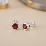 Sterling silver stud earrings with round natural garnet stones, displayed on a beige surface.