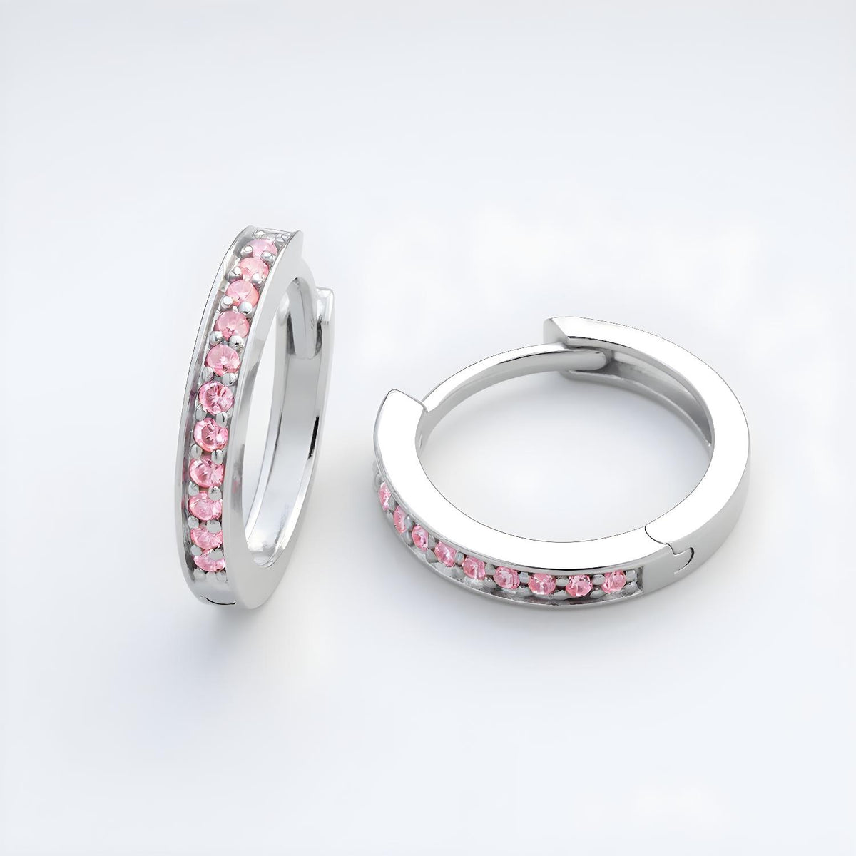 Silversmiths sterling silver huggie hoops with pink cubic zirconia rest on a plain white surface.
