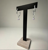 Sterling silver simulated alexandrite charm hoop earrings displayed on a black T-stand with a wood base.