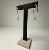 Sterling silver hoop earrings with simulated London topaz charms displayed on a black T-stand with a wood base.