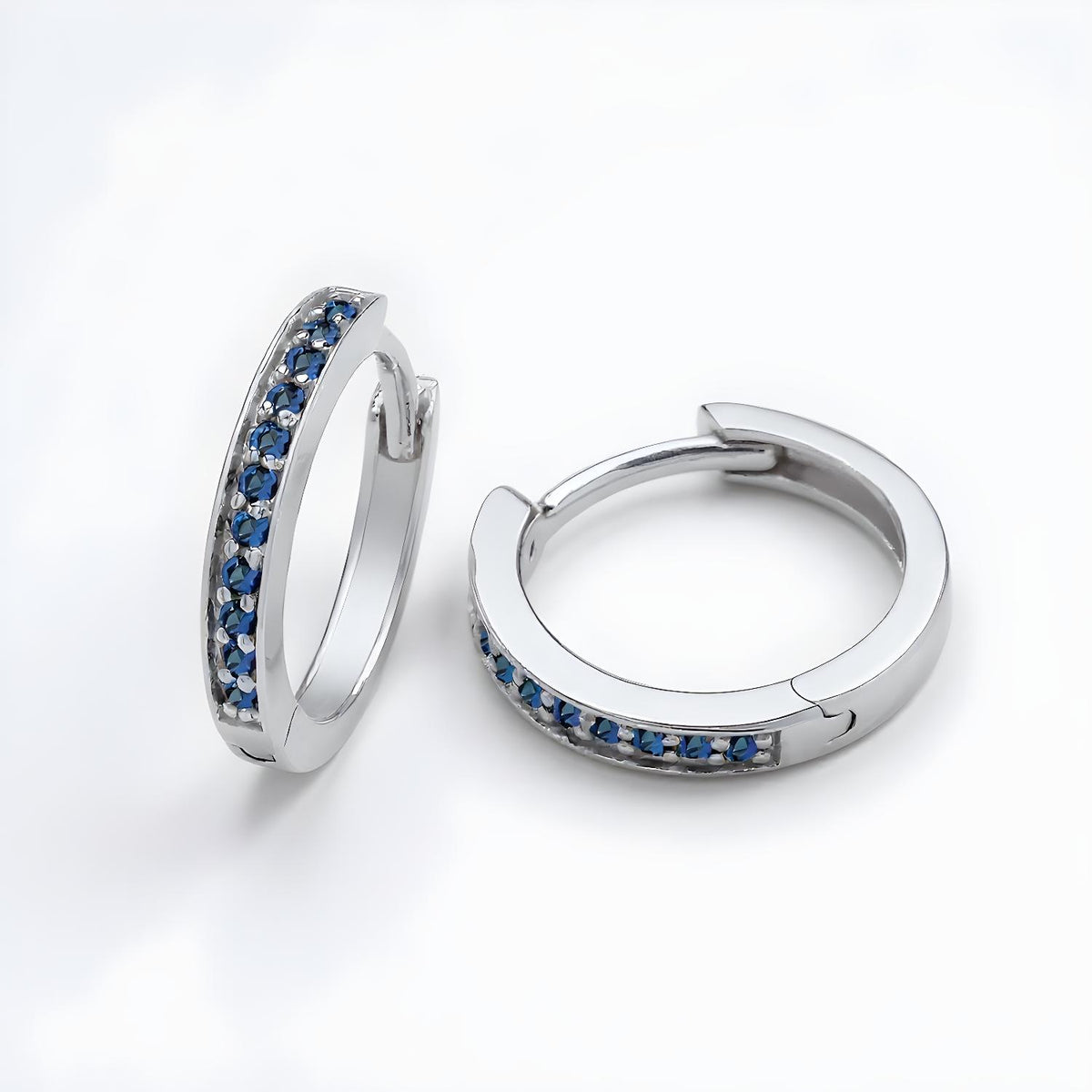 Silversmiths sterling silver huggie hoop earrings with simulated sapphires on a plain white background.