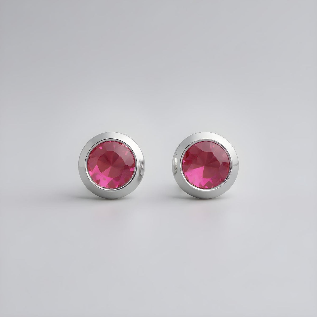 Sterling silver stud earrings with bezel-set simulated rubies on a minimalist light gray background.