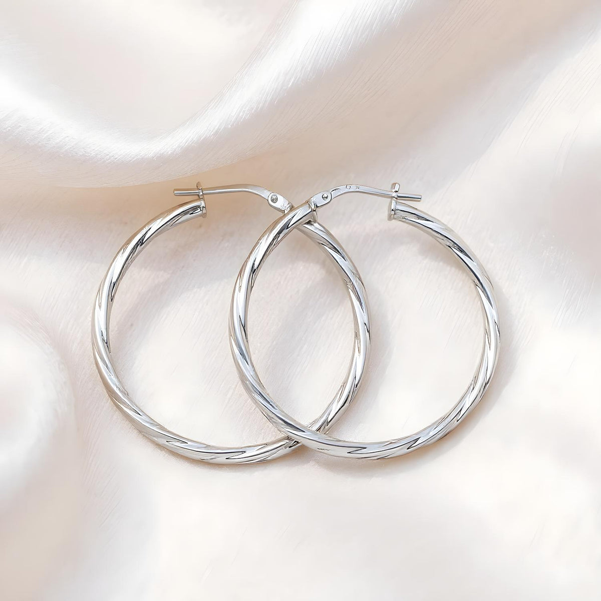 Silversmiths Sterling Silver 45mm twist hoop earrings displayed on satin fabric, reflecting their polished shine.