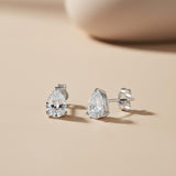 A pair of Silversmiths 7x5mm sterling silver teardrop CZ stud earrings, one standing upright on a beige surface.