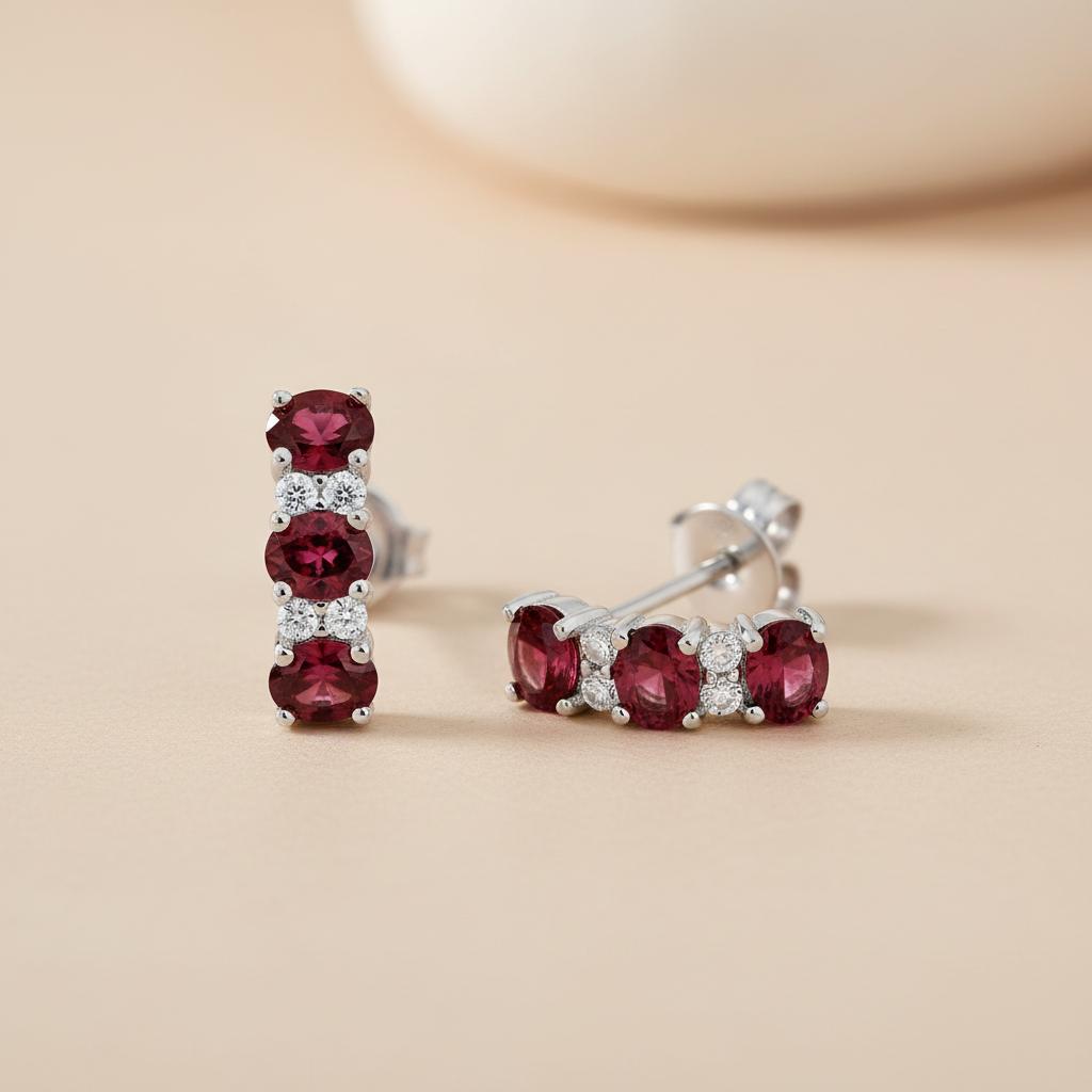 Sterling silver drop stud earrings with three simulated rubies and clear stones on a beige background.