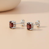 Sterling silver stud earrings with oval natural garnets shown on a light beige surface.