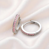 Silversmiths sterling silver huggie hoops with pink cubic zirconia rest on a soft, light-colored fabric.