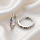 Sterling silver huggie hoops with rainbow cubic zirconia rest on smooth white silky fabric.