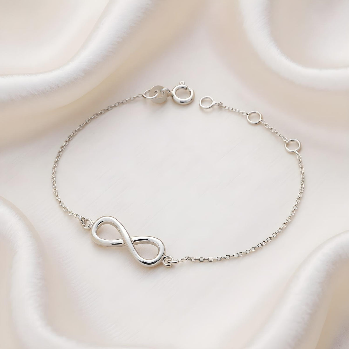 A sterling silver infinity station bracelet with adjustable links is shown on white fabric.
