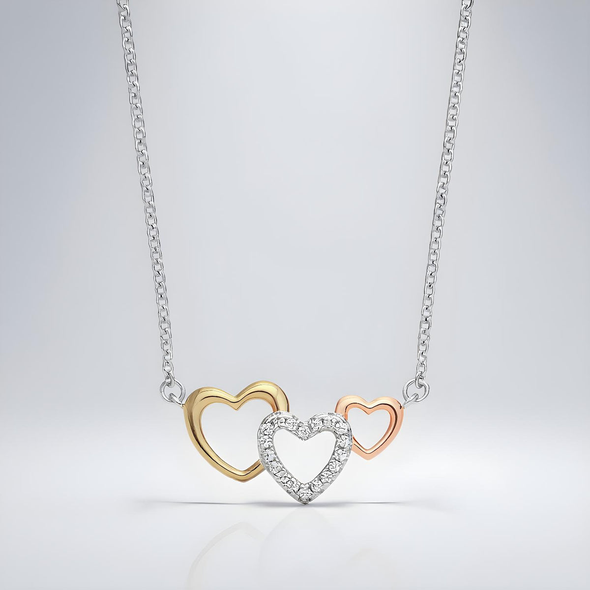 A sterling silver necklace with rose and yellow gold triple heart cubic zirconia pendant on a plain background.