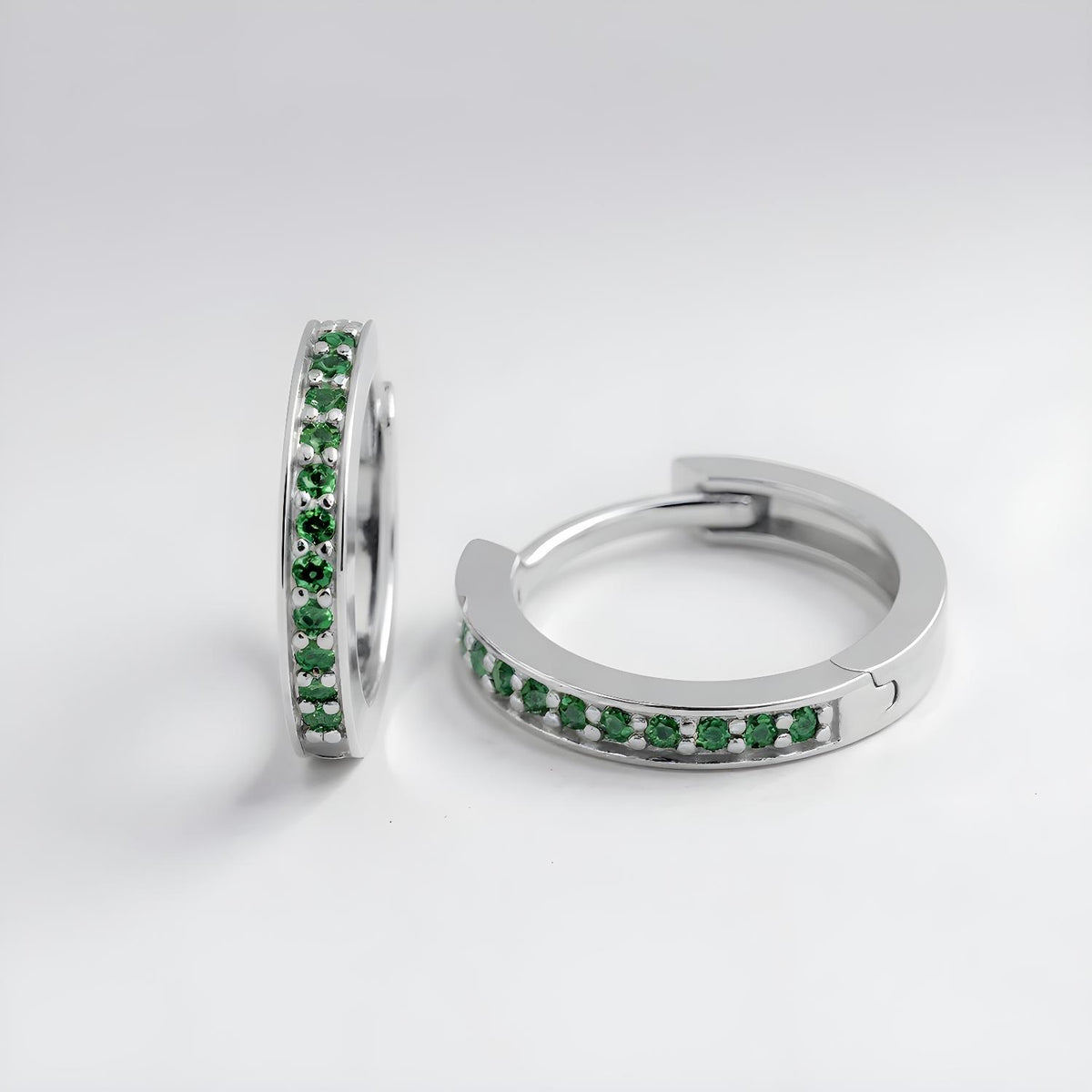 Sterling silver huggie hoops with a row of green simulated emerald stones, displayed against a white background.
