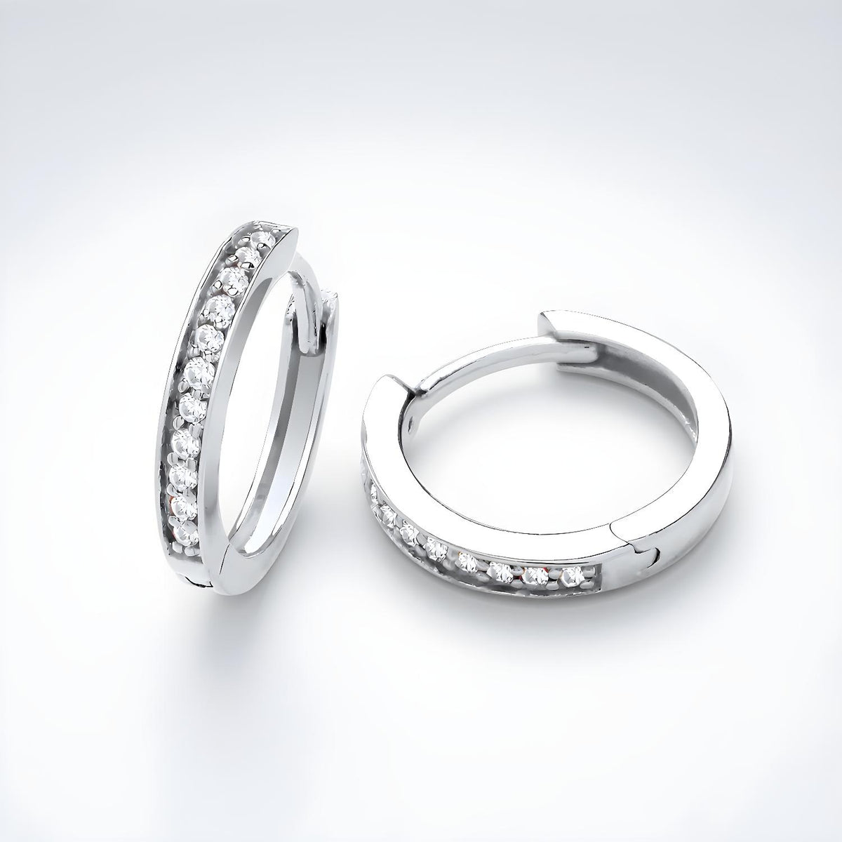 Silversmiths sterling silver pavé cubic zirconia huggie hoops with clear stones in front, displayed on a white surface.
