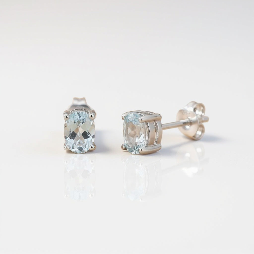 Silversmiths sterling silver stud earrings with oval blue topaz stones set on a plain white background.