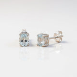 Silversmiths sterling silver stud earrings with oval blue topaz stones set on a plain white background.