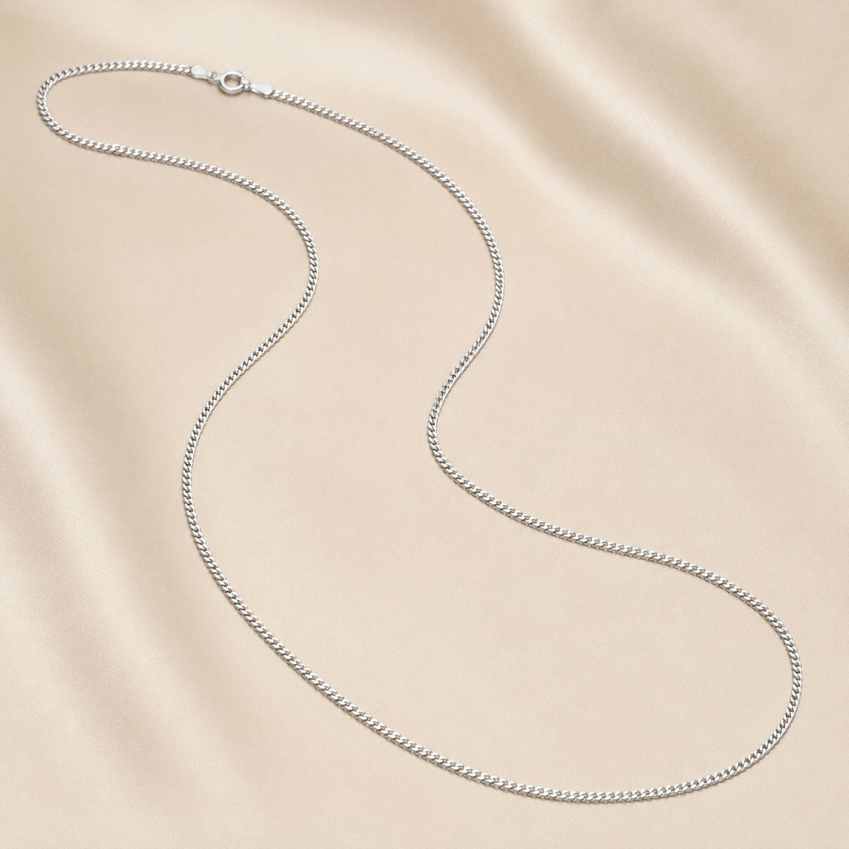 A woman in a green blouse wears two silver necklaces, one with a heart-shaped pendant and the other a simple chain. She holds the pendant necklace with her left hand. Her face is partially visible.