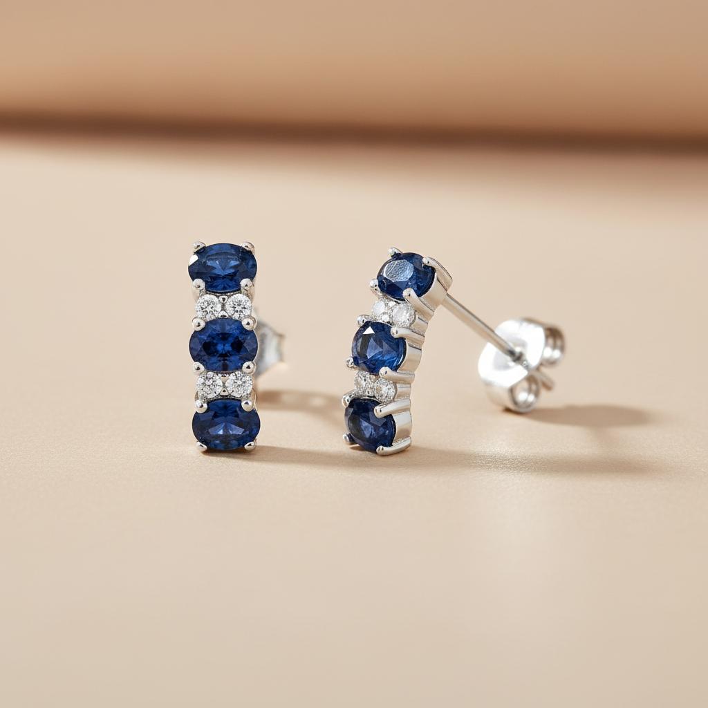 Silversmiths sterling silver drop stud earrings with simulated sapphire and CZ, displayed on a beige background.