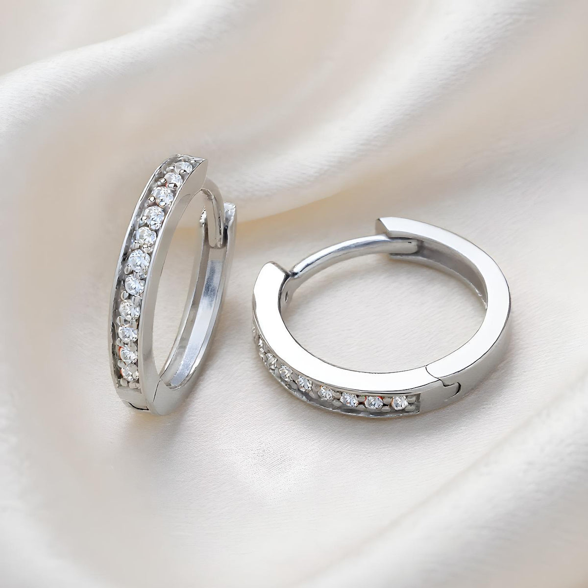Sterling silver pavé cubic zirconia huggie hoops from Silversmiths displayed on a soft, light background.