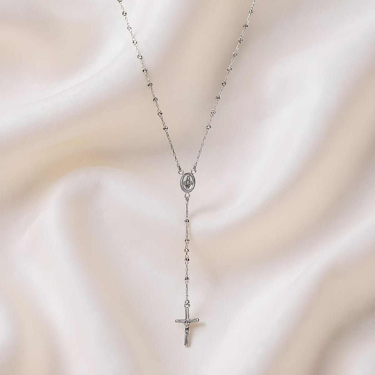 A 24-inch Silversmiths sterling silver rosary bead cross necklace on a pale fabric background.