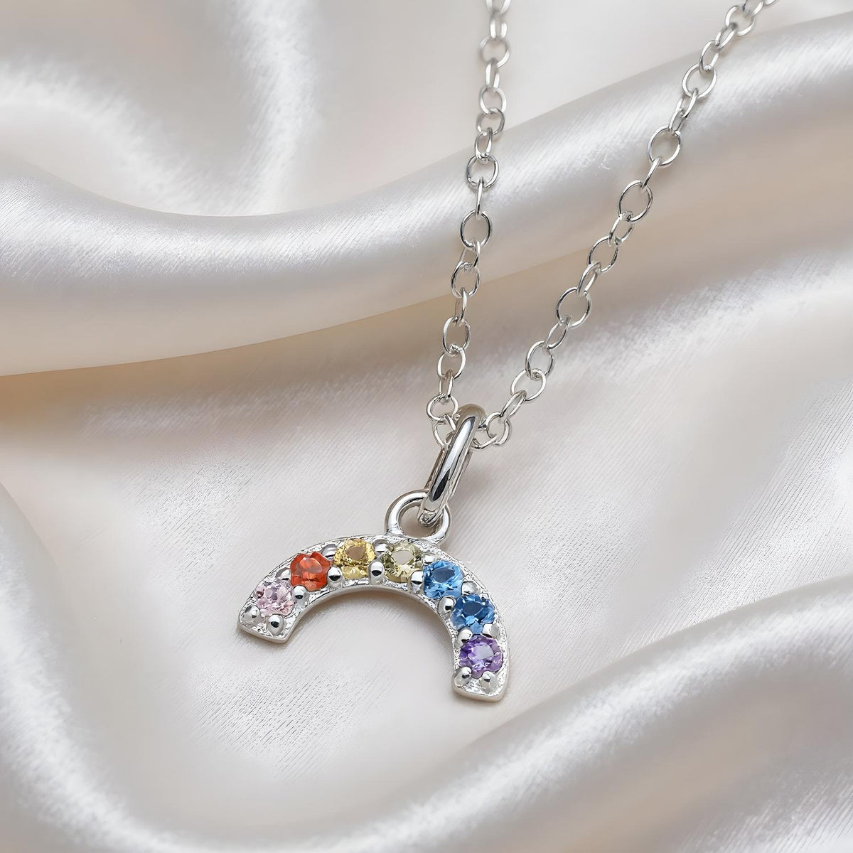 A sterling silver crescent moon necklace with rainbow cubic zirconia rests on white satin fabric.