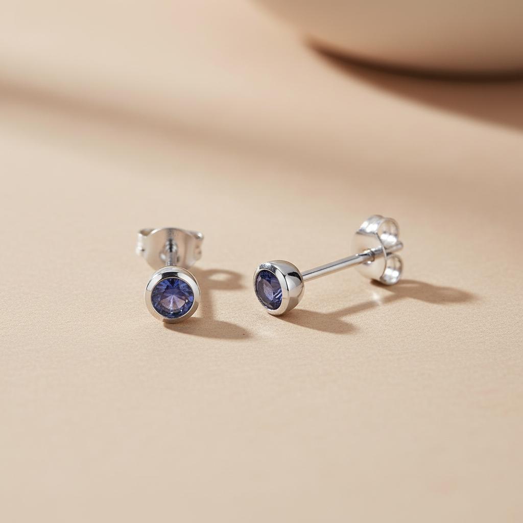 Silversmiths sterling silver stud earrings with 4mm simulated tanzanite displayed on a beige surface.