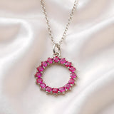 Silversmiths sterling silver necklace with a simulated ruby circle pendant rests on white satin fabric.