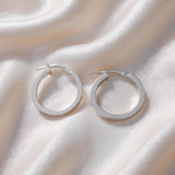 Silversmiths Sterling Silver 28mm plain oval hoop earrings shown on a white satin background.