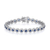 A sterling silver tennis bracelet with 6.5mm sapphires and CZ halos, shown with secure clasp on a white background.