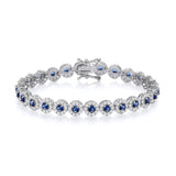 A sterling silver tennis bracelet with 6.5mm sapphires and CZ halos, shown with secure clasp on a white background.