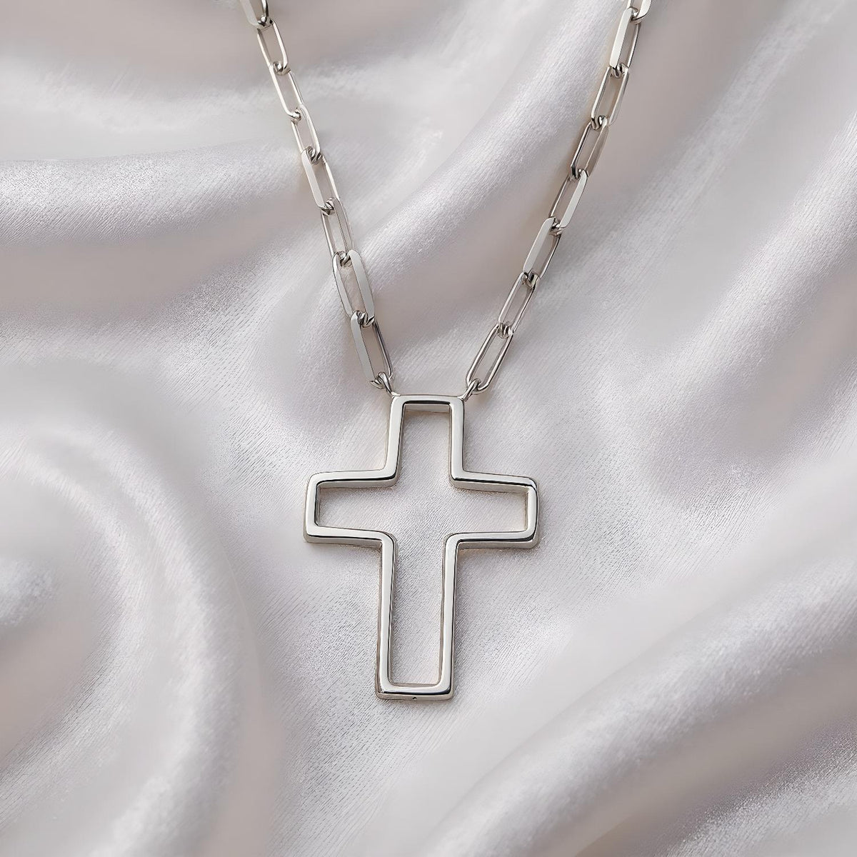 A sterling silver open cross paperclip chain necklace rests on soft white satin fabric.