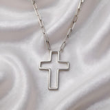 A sterling silver open cross paperclip chain necklace rests on soft white satin fabric.