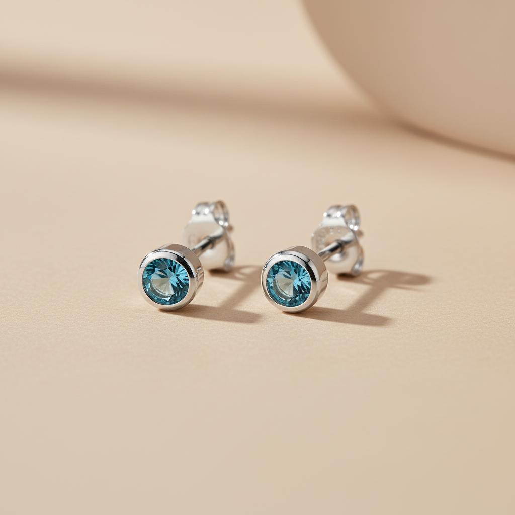 Silversmiths sterling silver stud earrings with simulated London topaz set in bezels on a smooth beige surface.