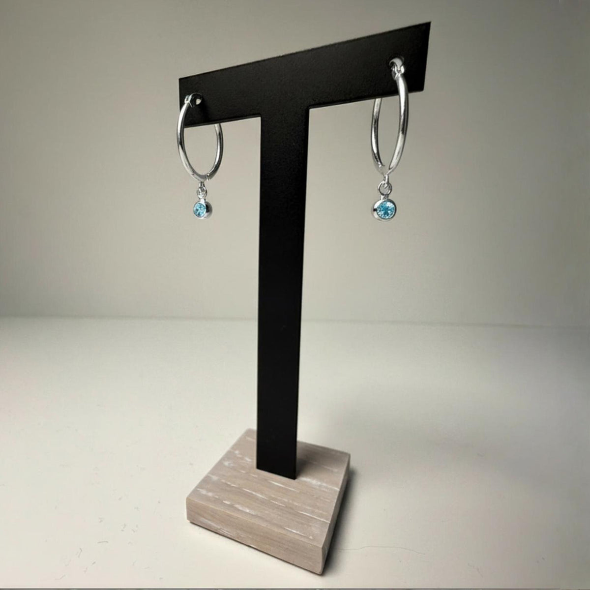 Silversmiths silver hoops with simulated aquamarine stones for March, shown on a black T-stand.