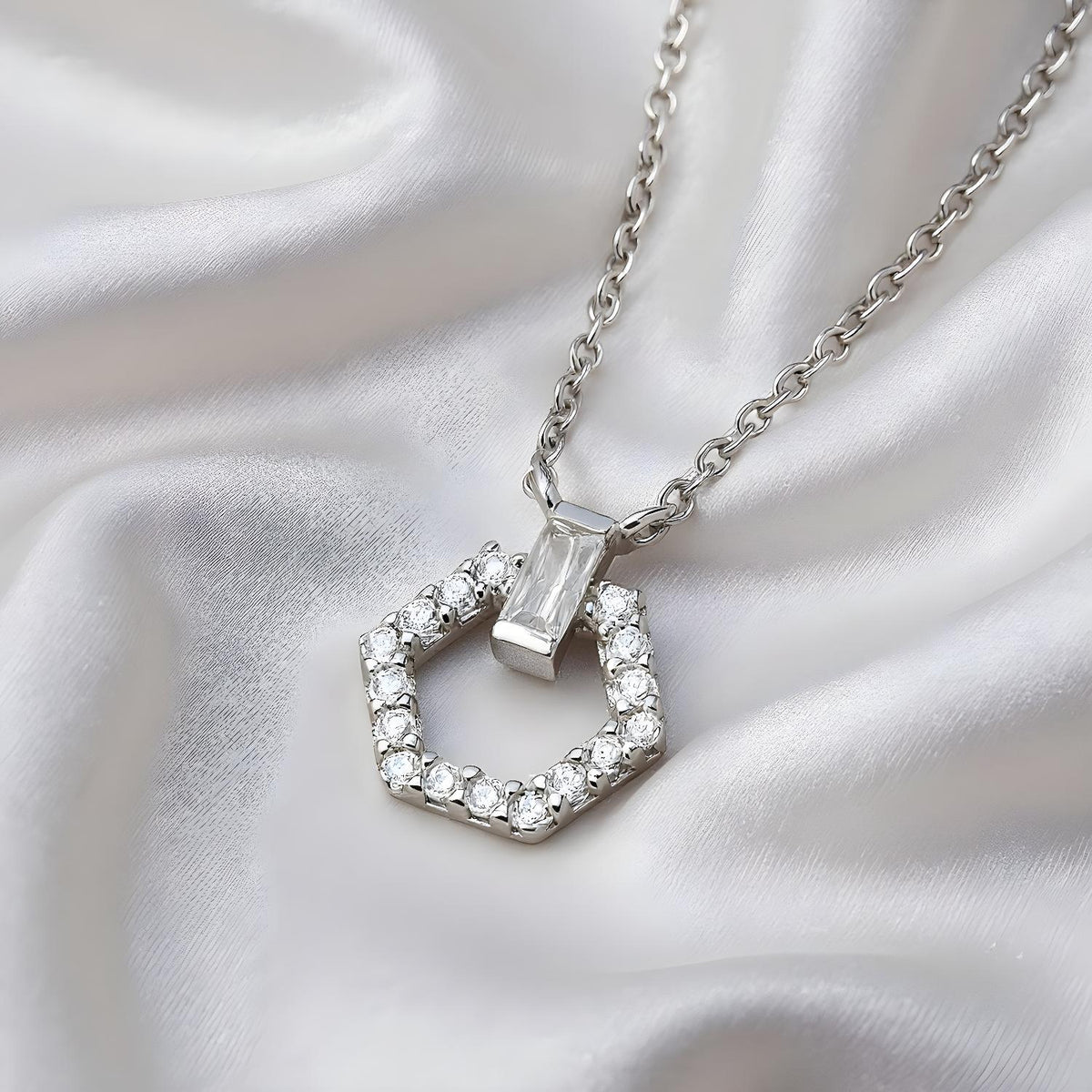A sterling silver necklace with a cubic zirconia hexagon pendant is displayed on white satin.