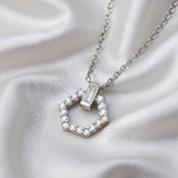 A sterling silver necklace with a cubic zirconia hexagon pendant is displayed on white satin.