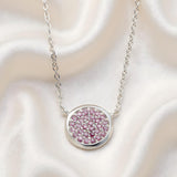 A Sterling Silver necklace with simulated ruby circle clusters lies on cream satin fabric.
