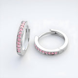 Silversmiths sterling silver huggie hoops with pink cubic zirconia rest on a plain white surface.