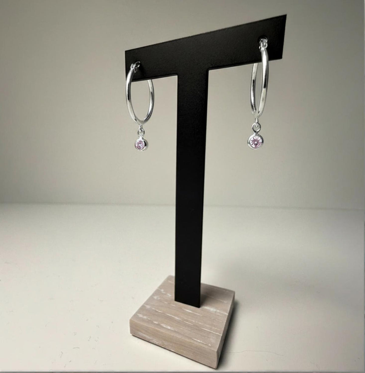 Sterling silver simulated alexandrite charm hoop earrings displayed on a black T-stand with a wood base.