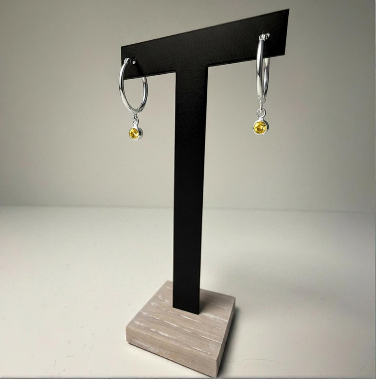 Sterling silver simulated citrine hoop earrings displayed on a black T-stand with a wooden base.