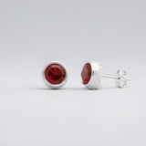 Silversmiths sterling silver stud earrings with natural garnet stones on a light gray background.